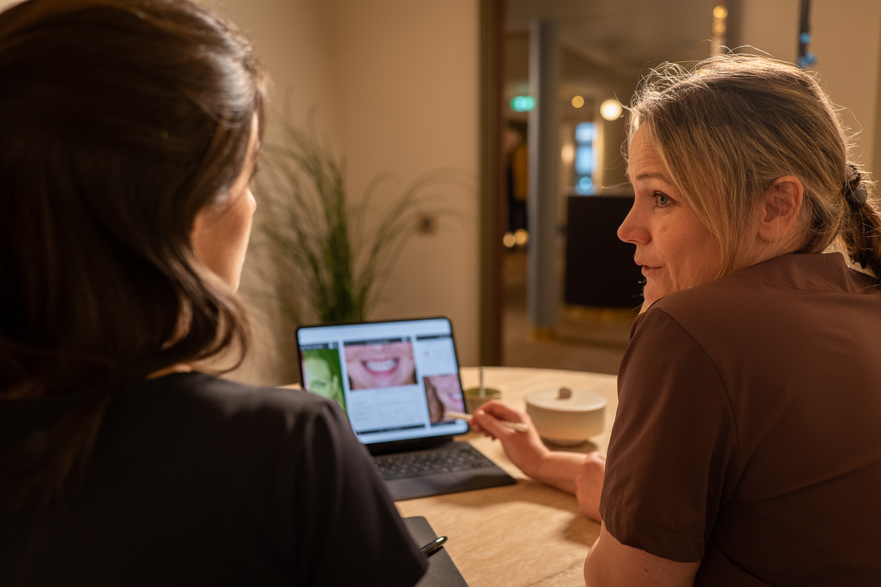 Tannlege forklarer et smilforslag på et nettbrett mens pasienten sitter ved bordet
