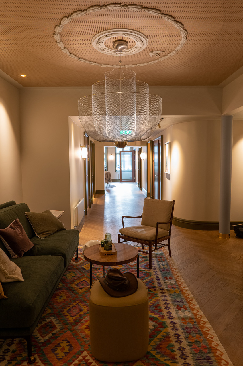 Lounge hos Vinci Dental Studio med grønn sofa, mønstret teppe, rundt sofabord i tre og stor pendellampe i taket